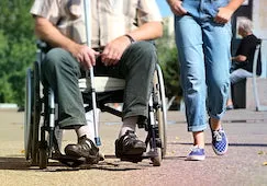 Man in wheelchair beside woman in blue jeans who is walking